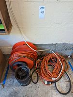 Full view of the large orange and black shop extension cords coiled and piled on the floor against a wall.