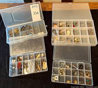 Four plastic compartmentalized boxes filled with assorted costume jewelry pieces including earrings, pins, bracelets, and necklaces.