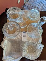 Photo showing entire collection on beige cloth including cut glass bowl, lidded candy bowl, decanter with stopper, cheese plate with bell cover, cruets, and additional dishes.