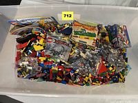 Large plastic bin containing loose LEGO pieces, instruction manuals and polybags
