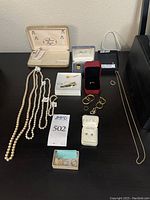 Overview of all lot items on black surface: pearl strands, earrings, chain, boxes, cufflinks, ring and accessories