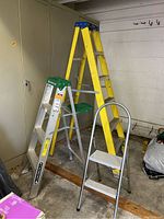 6-foot yellow A-frame ladder, 4-foot aluminum step ladder, and small 2-step stool ladder arranged in a garage corner.