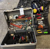 Metal toolbox opened showing organized hand tools inside, assorted wrenches, screwdrivers, pliers, hammer, scissors, and respirator mask on side