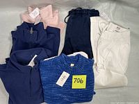 Lot overview of all clothing items folded including 2 fleece tops, sweater, white pants, and navy jeans.
