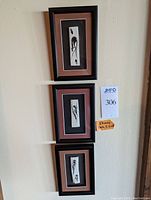 Full view of three framed Aboriginal paintings hung vertically on a wall with lot number and size note visible