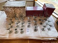 Front view of 22 smoky colored stemware glasses including 11 coupes and 11 wine glasses with fabric storage containers behind.