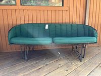 Front view of metal framed outdoor rocking couch with green cushions on wooden deck.