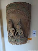 Full view of the wood relief carving showing two seated figures with headdresses and an ornamental arched border above them.