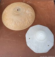 Two antique glass ceiling shades placed side by side on a brown surface, showing patterns and central mounting holes.