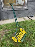 Overall angled view of the restored antique Mars Turf King push reel mower showing yellow reel, wheels, green frame, and wooden handle grips.