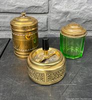 Antique smoking accessories including two humidors and one art deco rotary ashtray arranged on a dark surface.