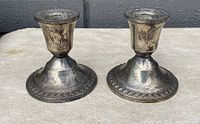 Pair of antique sterling silver weighted candlesticks with flared bases and decorative rim, showing light tarnish and surface wear.