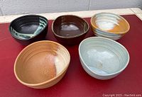 Five vintage pottery bowls arranged on a red surface; various colors and complementary glazes visible.