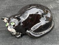 Top view of glossy black and white cat figurine showing curled position and green eyes.