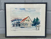 Framed watercolor painting showing a house in winter landscape with red roof and surrounding trees in soft colors.