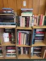 Boxes filled with numerous hardcover books covering art, fiction, cooking, and atlas topics.