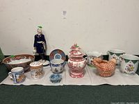 Full view of all items arranged on cloth: figurine, bowls, mugs, jars, cachepots, and tureen