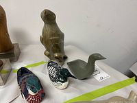 Group photo of two soapstone bird carvings and two painted wood duck figurines laid on a white cloth with green tape lines.
