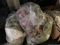 Four large clear plastic bags filled with green and pink floral patterned custom fabric curtains and drapes, some with cream fabric sections visible.