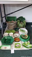 Overview of mixed green ceramic plates, bowls, mugs and vases arranged on table under cart