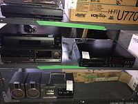 Full view of two Sony Beta HiFi VCRs and Sony DVD CD player on metal shelving with cardboard boxes in background