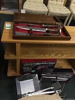 Antler-handled grilling tool set in wooden case alongside grilling basket, tongs, thermometer and boxed grilling basket system on a wooden table