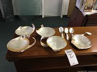 Four mother of pearl shell bowls and four spoons displayed on a wooden surface, showing the iridescent quality and footed bases of the bowls.