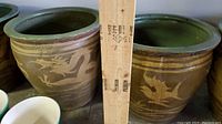Photo showing two brown ceramic planters side by side with detailed beige dragon and bird designs, a wooden ruler between them for scale, and green glazed interior rims visible.