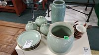 Full view of celadon green pottery plates, vases, and mini urns assembled together with Hall soup bowls nearby