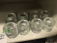 Six clear textured glass holders arranged on a shelf, three in front and three in back, some with tealight candles inside.