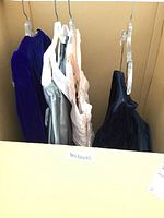 Four gowns hanging in cardboard staging box labelled “Ballgowns”