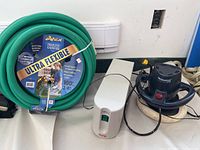 Photo showing the lot items side by side: green coiled Apex garden hose with label, white APC Power Cell device, and black Waxmaster electric polisher with cords.