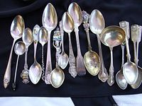 Row of varied sterling silver spoons on black background including souvenir and ornate designs