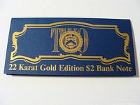 Blue display folder with gold embossed text and emblem reading '22 Karat Gold Edition $2 Bank Note'.