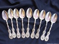 Nine ornate sterling silver spoons laid out on dark cloth