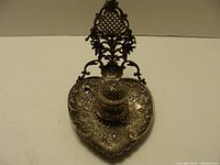 Top view of ornate heart-shaped ink well with pen holder showing floral engravings and lattice design.
