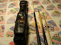 Full lot setup showing three pool cues and carrying case on quilted background.