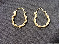 Pair of twisted rope style hoop earrings in 10K gold displayed on black fabric.