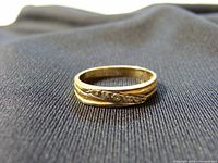 Close-up of 14K yellow gold ring with engraved leaf and vine design on band against dark fabric background