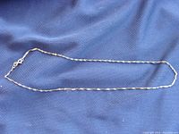 Full view of the gold twist style chain necklace laid flat on blue fabric to show full length and style.