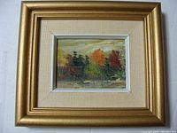 Framed oil painting showing autumn landscape scene with trees in multiple colors and textured beige mat with gold frame.