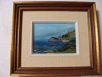 Framed oil painting with wooden piers, boats, buildings, and coastal landscape in muted colors.