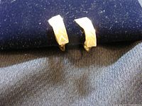 Pair of lightweight 10 kt gold earrings with engraved chevron motif displayed on dark fabric background.