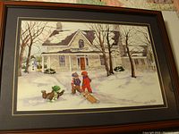 Framed watercolor showing a winter scene with three children playing outside a snow-covered stone house with bare trees and a snowman.