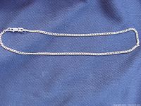 Full view of the small gold chain laid out on a dark fabric background, showing the chain's length and design.