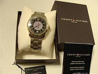 Tommy Hilfiger watch displayed on cushion inside original box with instruction manual beside it.
