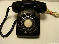 Top view of vintage black rotary dial telephone showing dial plate with letters and numbers, handset with coiled cord, and main body.