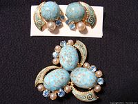 Pair of oval turquoise blue Carbachon stone clip-on earrings accented with small pearls and blue rhinestones, set with gold-tone and turquoise enamel scroll design.