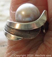 Close-up of the ring worn on finger showing the design and pearl detail.