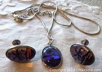 Front view of pendant and earrings showing blue translucent butterfly wing with black palm tree design and orange accents in silver tone settings.